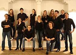 Schwarz gekleidete Mitgleider des Folkwang Vokalensemble in verschiedenen Posen vor weißem Hintergrund 