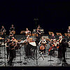 Musikensemble mit Instrumenten auf einer Bühne mit schwarzem Hintergrund