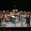Musikensemble mit Instrumenten auf einer Bühne mit schwarzem Hintergrund