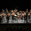 Musikensemble mit Instrumenten auf einer Bühne mit schwarzem Hintergrund