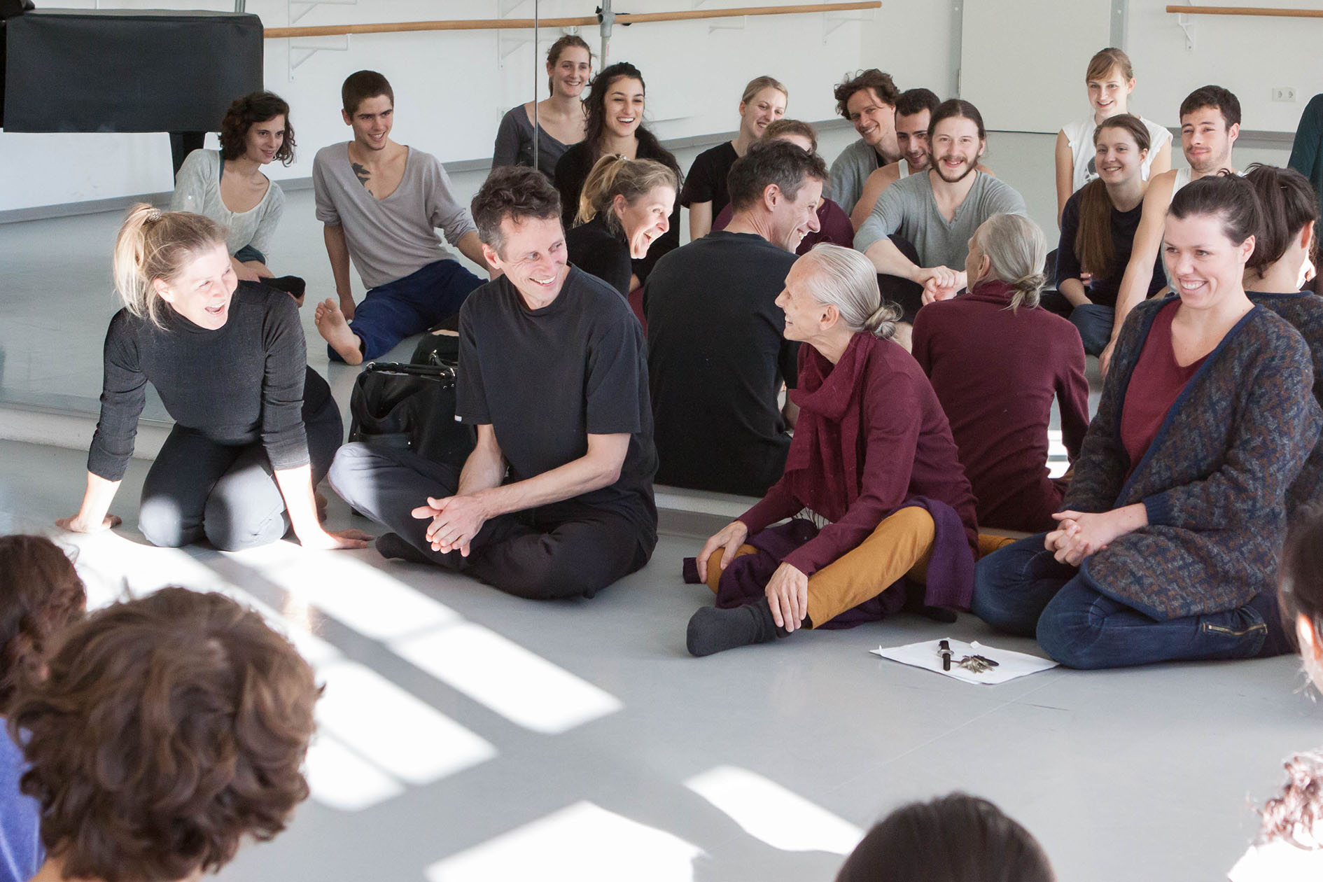 Tänzer*innen in einem Kreis auf dem Boden eines weißen Tanzstudios sitzend